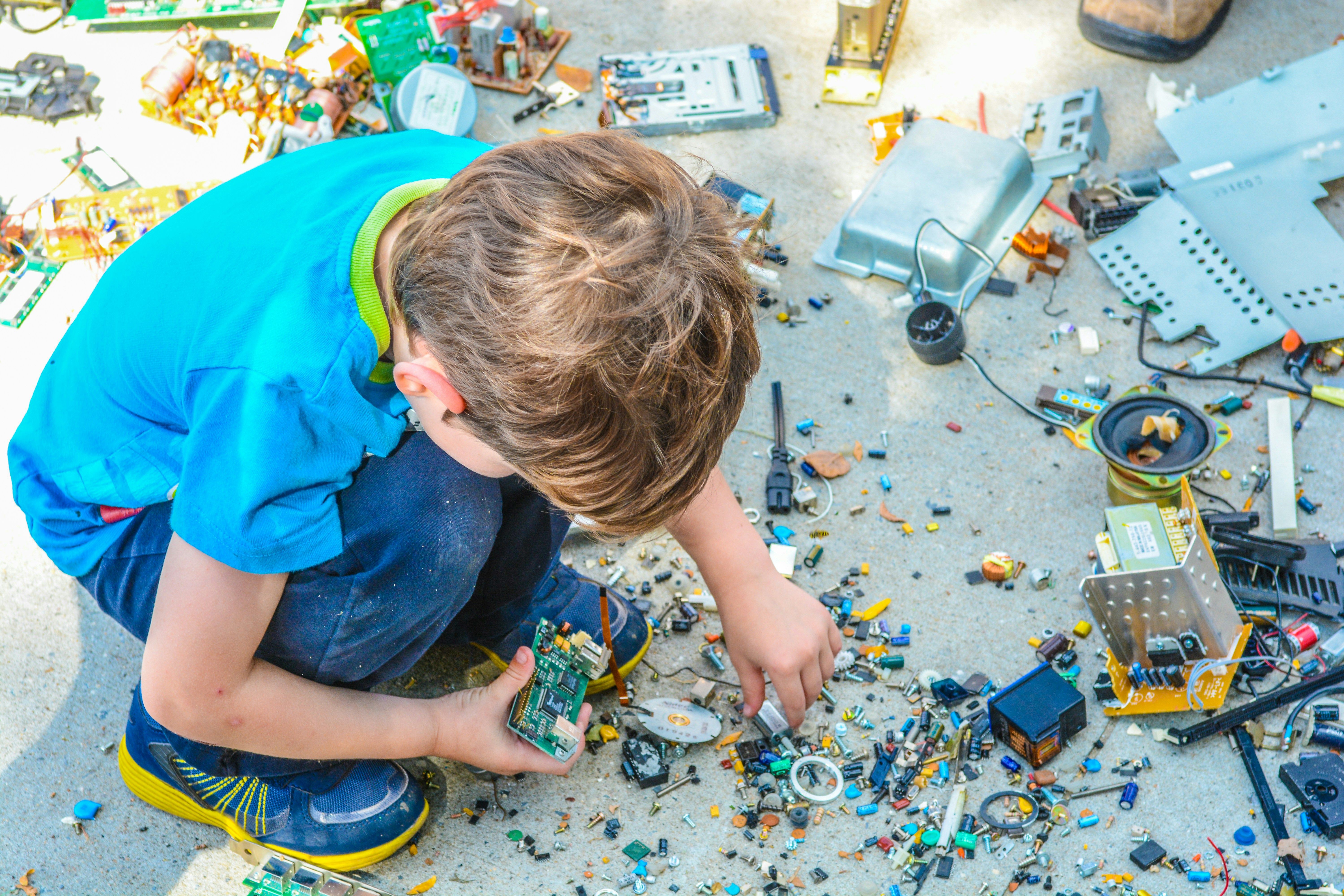 Child taking apart old electronics, with circuit boards and parts spread on the ground