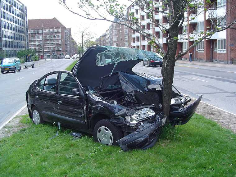 Photo of car accident with a black car crashed into a tree. The car is heavily damaged.